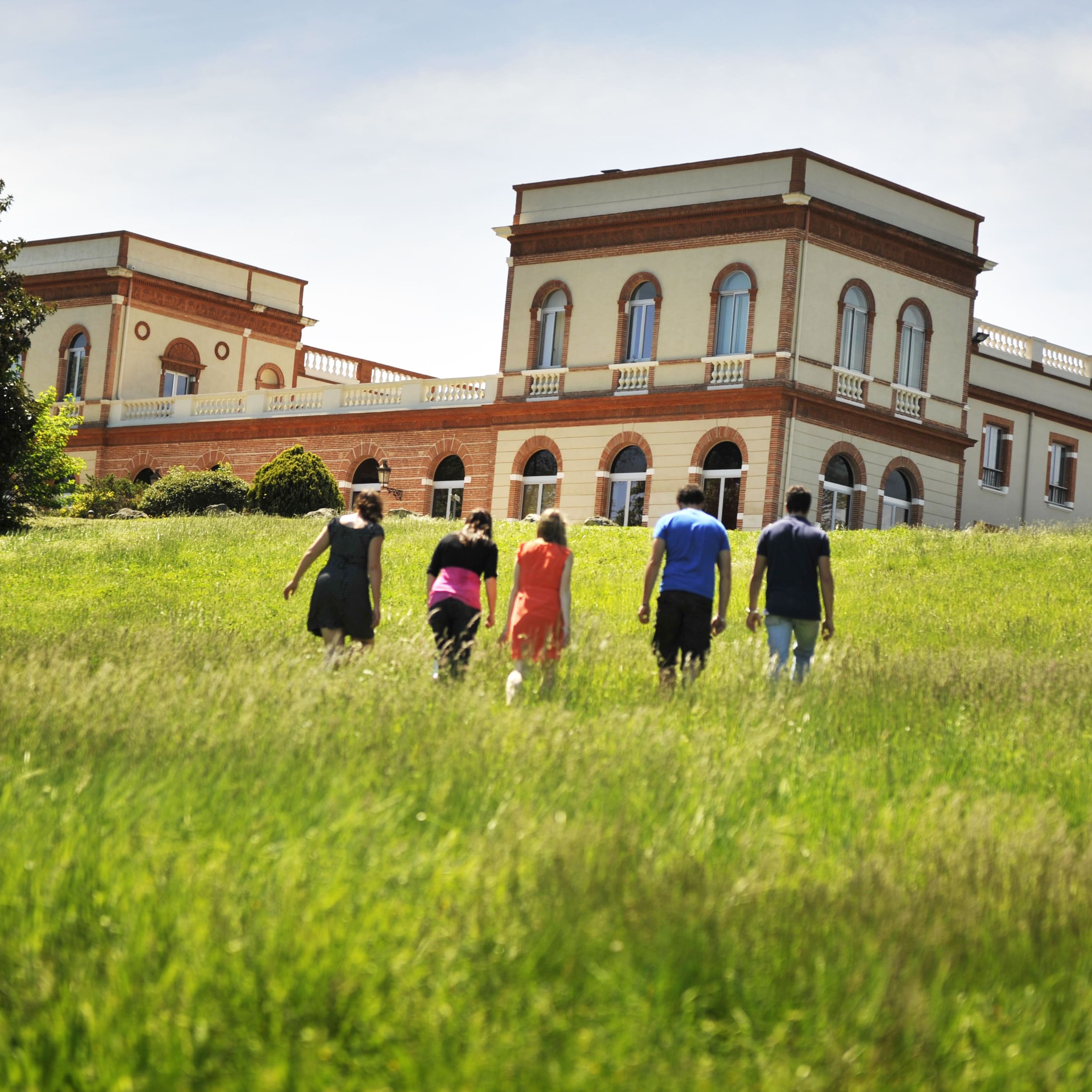 Un groupe de personnes marche dans une prairie en direction du Château de Purpan, sous un ciel bleu et ensoleillé. Un groupe de personnes marche dans une prairie en direction du Château de Purpan, sous un ciel bleu et ensoleillé.